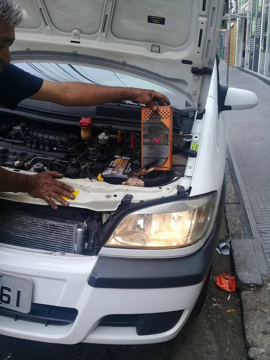 Mecânico debruçado sobre o vão do motor aberto de um carro branco durante um serviço elétrico